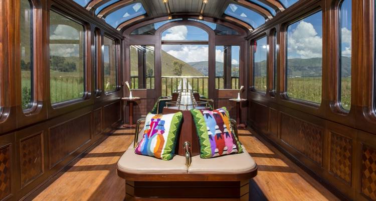 Vagón de tren con cojines coloridos y ventanas amplias que muestran el paisaje.