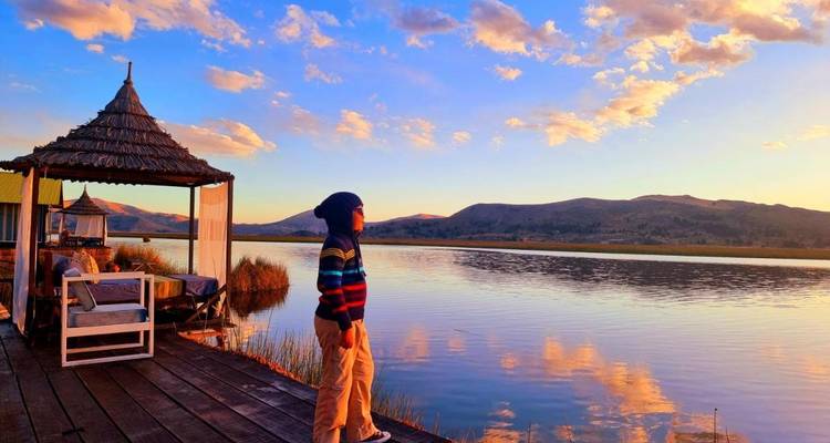 Person standing on a dock during sunset by a lake.