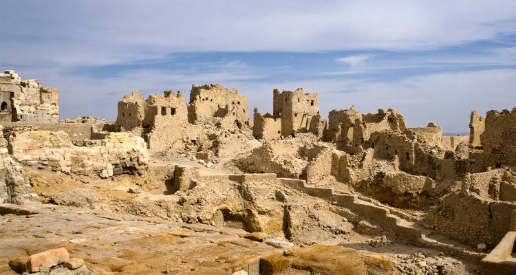 Ruines d'une forteresse du désert avec un terrain rocheux sous un ciel bleu.