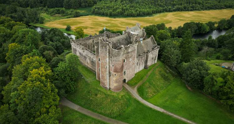 Luftaufnahme einer großen historischen Burg, umgeben von üppigem Grün.