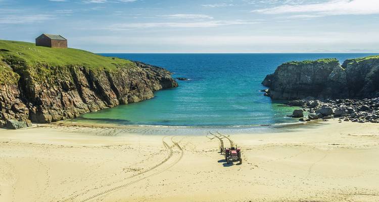 Secluded sandy beach with turquoise cove bordered by rocky cliffs and grassy headland.