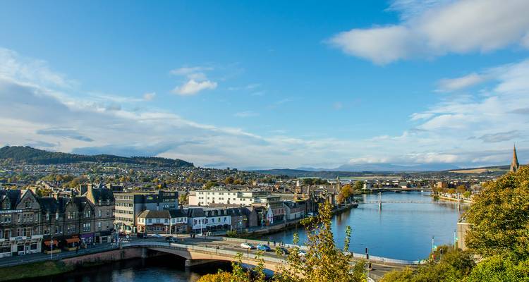 Stadsgezicht van Inverness aan de rivier met een brug over de River Ness onder een heldere blauwe hemel.