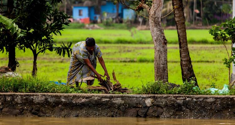 Woman working by a canal with green fields in the background.
