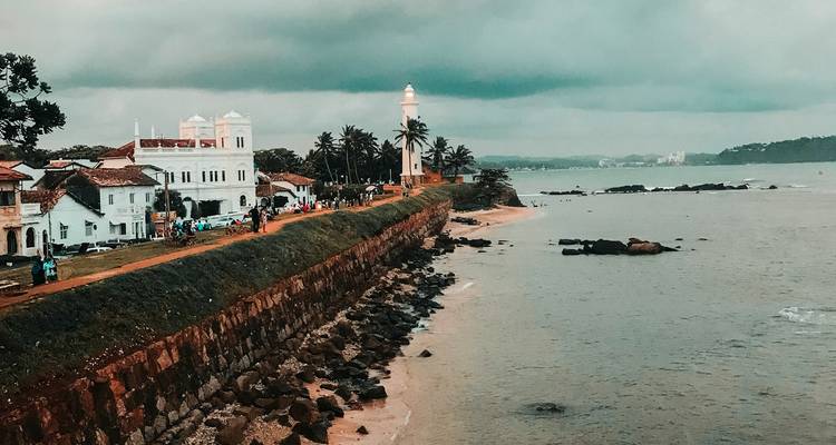 Een kustgezicht met een vuurtoren en koloniale gebouwen.