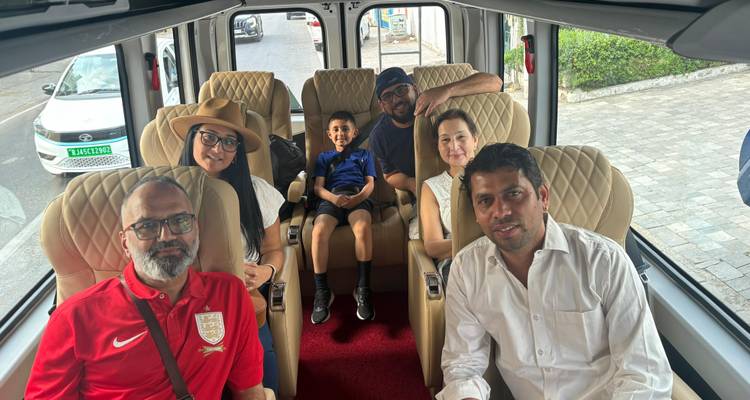 Groep van zes mensen in een bus, glimlachend naar de camera.