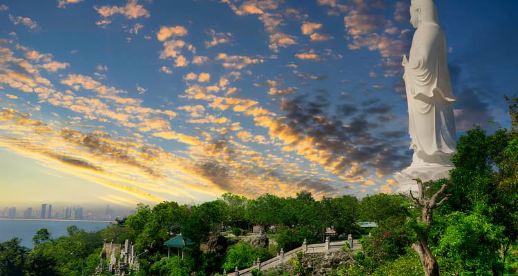 Large statue overlooking a city with a dramatic sky.