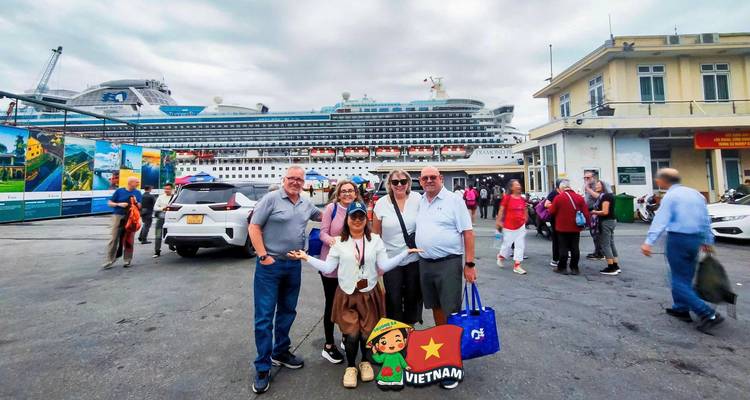 Los pasajeros del crucero sonríen frente a un imponente barco de crucero atracado en el puerto.