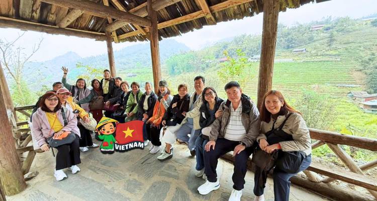 Gran grupo descansa bajo un refugio de madera con vista a campos en terrazas y colinas.