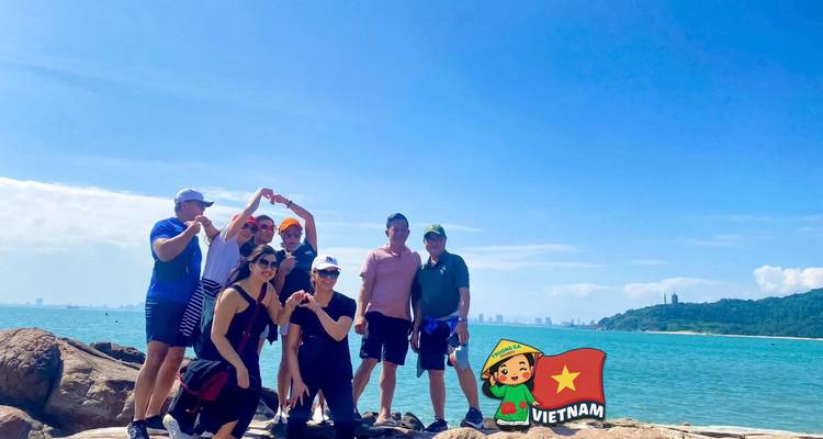 Grupo posa sobre rocas junto al mar con agua turquesa y horizonte a la distancia.