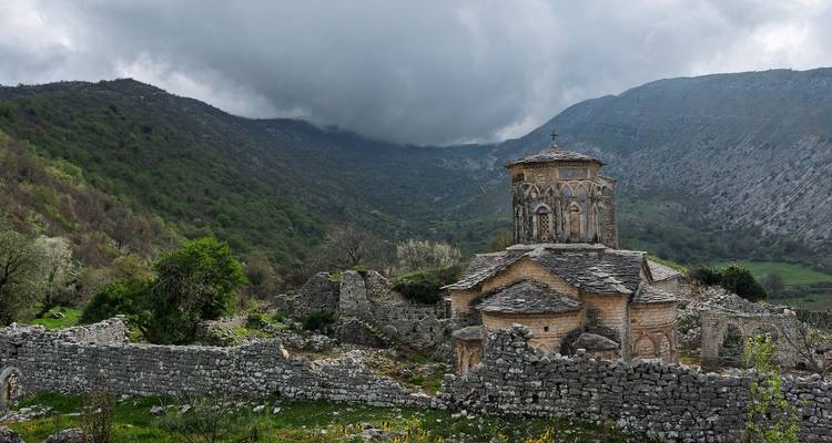 Une église de pierre historique entourée de ruines et située dans un paysage montagneux.