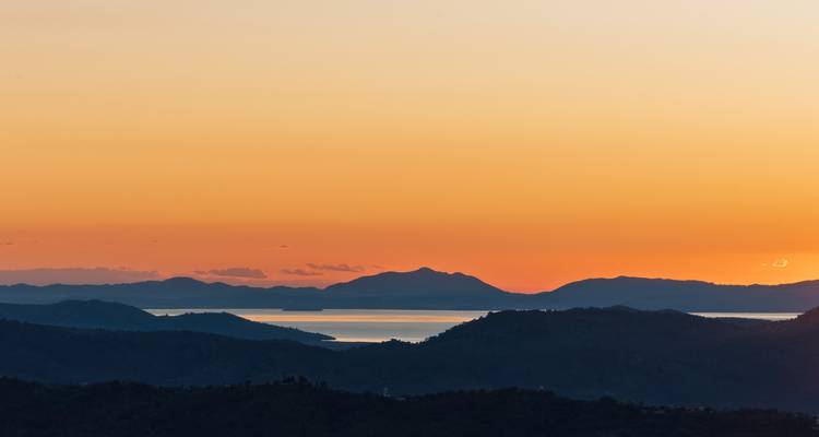 Vue du coucher de soleil sur une chaîne de montagnes avec une mer lointaine.