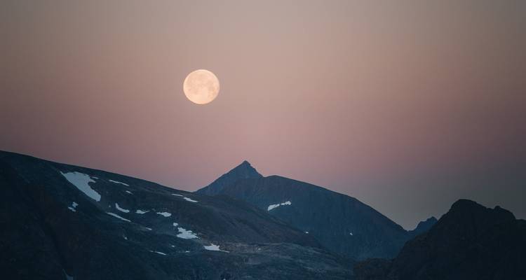 Full moon over a mountain at dusk.