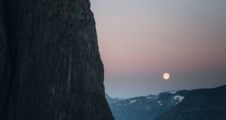 Moon rising beside a cliff.