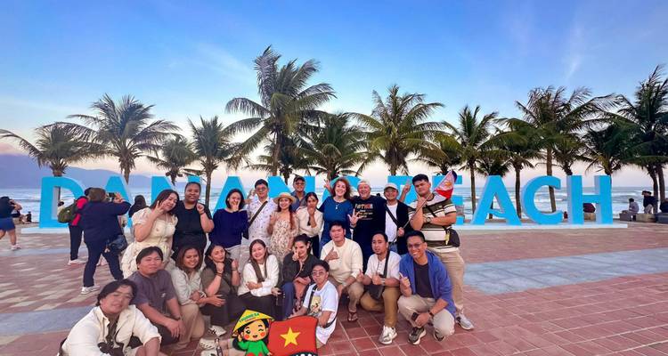 Groep mensen poseren voor het Da Nang Beach bord met palmbomen.