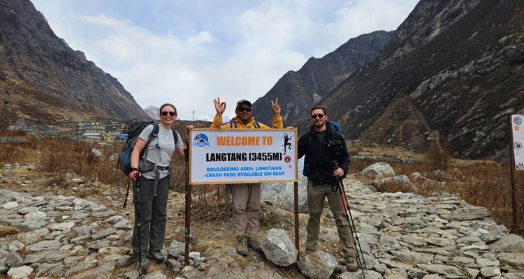 Groupe de randonneurs posant devant le panneau de Langtang, montagnes en arrière-plan.
