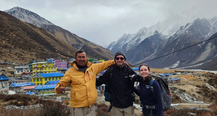 Trois personnes posant avec des bâtiments colorés et des montagnes.