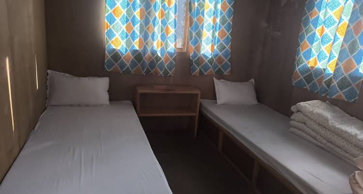 Hébergement simple avec deux lits et rideaux colorés.