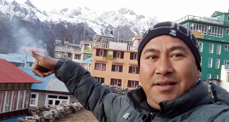 Homme pointant vers un village avec des montagnes en arrière-plan.