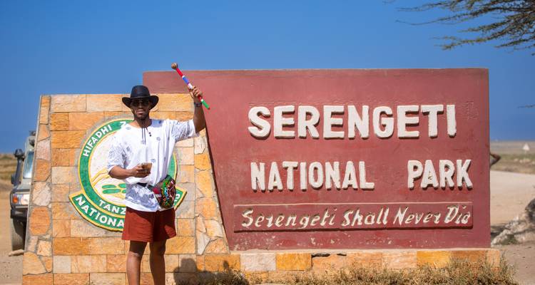 Visiteur posant près du panneau d'entrée du parc national du Serengeti.