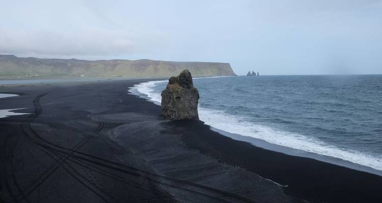 Black sand beach with rock formation in the water.