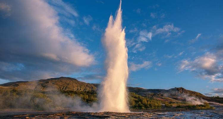 Geyser en éruption avec un ciel bleu et des nuages au-dessus.