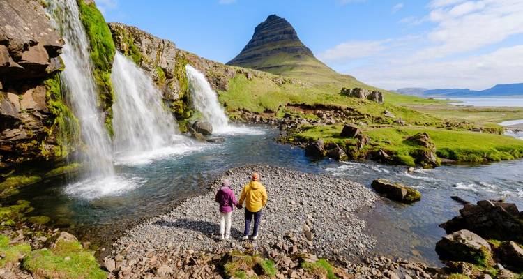 Deux personnes debout près d'une cascade avec une montagne en arrière-plan.