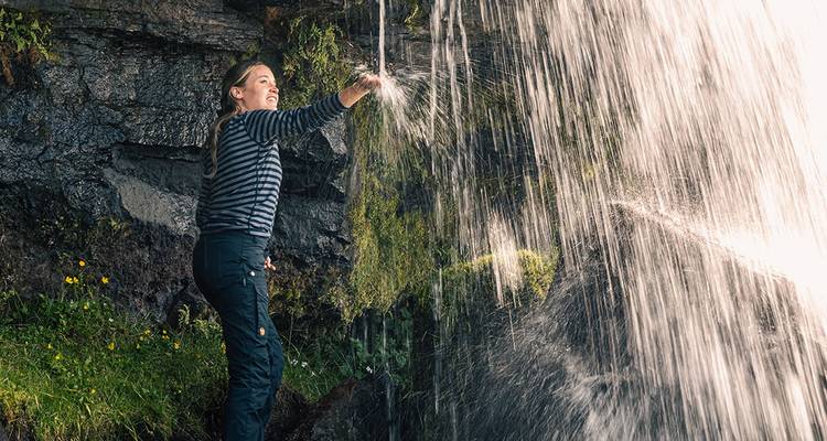 Person touching a waterfall with lush vegetation around.