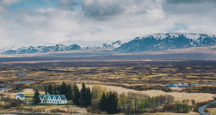 Countryside landscape with snowy mountains and a few scattered houses.