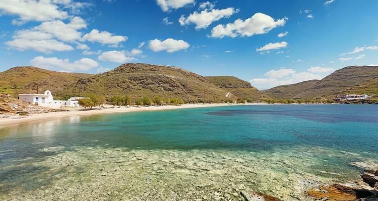 Quiet beach with clear, turquoise water and hills in the background.