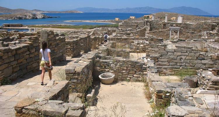Tourists walking among ancient stone ruins near the sea.