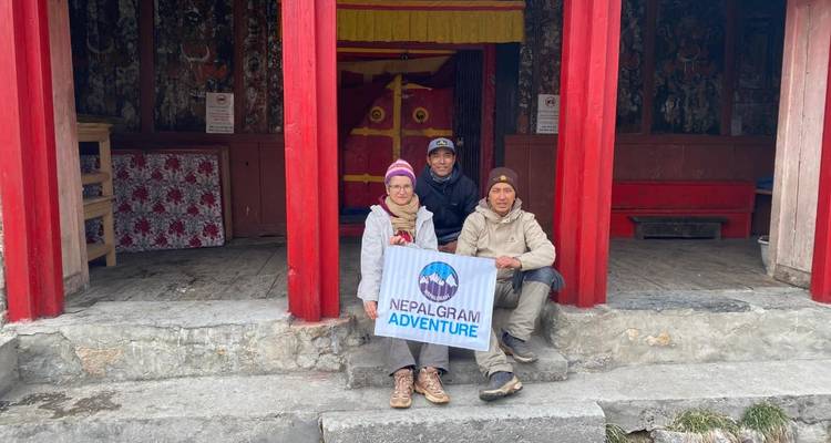 Trois personnes assises devant une structure rouge tenant une pancarte qui dit 'Nepal Gram Adventure'.