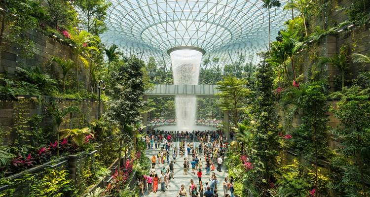 Vasto bosque tropical interior en el Aeropuerto Jewel Changi con una cascada imponente rodeada de plantas exuberantes y multitudes.