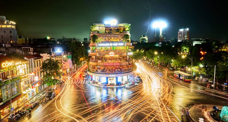 Vista nocturna de una intersección urbana concurrida con estelas de luz y edificios.