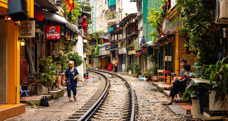 Vías de tren a través de una calle estrecha con edificios coloridos y gente.