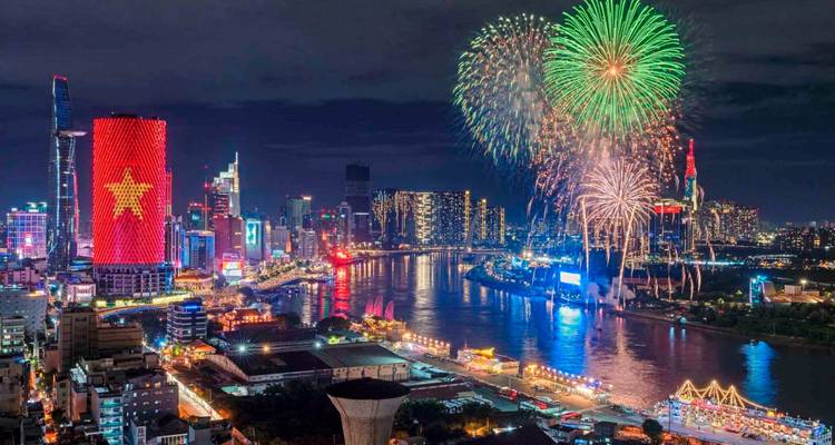 Vista nocturna del horizonte de la ciudad junto a un río con fuegos artificiales.