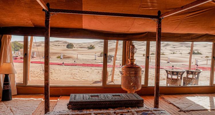 Interior view of a luxurious desert tent with traditional decor looking out onto sand dunes.
