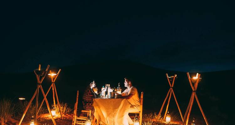 Couple dining at a candle-lit table in the desert at night.