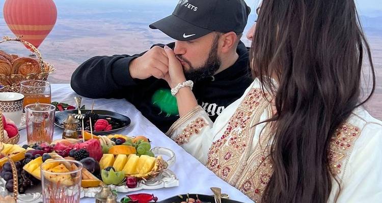 Couple enjoying a meal in a hot air balloon against a scenic landscape.