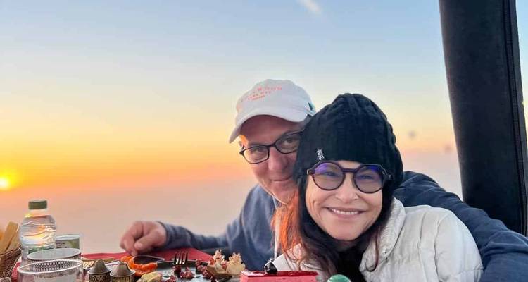 Couple smiling and posing in a hot air balloon with sunrise in the background.