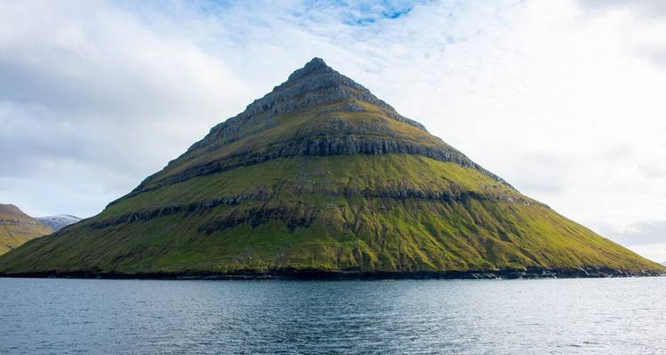 Montagne pyramidale s'élevant de la mer sous un ciel bleu.