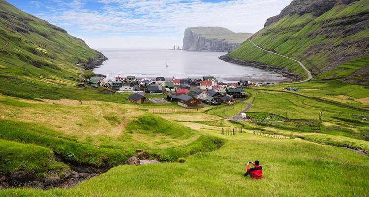 A scenic village surrounded by green hills and a view of the ocean with a person in the foreground.