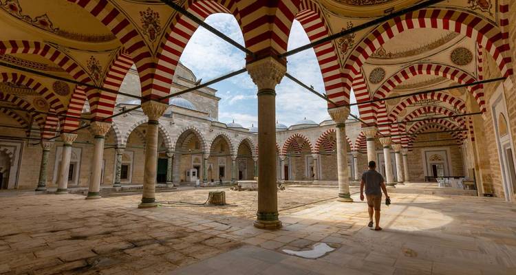 Personne marchant dans la cour d'une grande mosquée aux arcs rayés.
