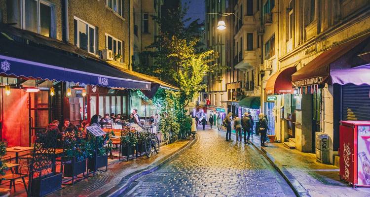 Scène de rue animée avec des gens profitant d'un dîner en plein air sur une rue pavée la nuit.