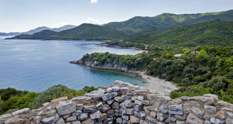 Mur de pierre surplombant un littoral pittoresque avec des montagnes et l'océan.