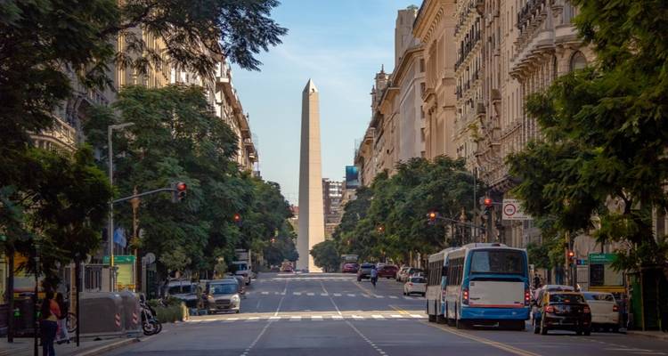A wide city street leading to the Obelisk of Buenos Aires, surrounded by tall buildings with trees lining the sides.