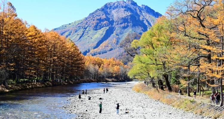 Personas disfrutando un día junto a un río con un telón de fondo montañoso.