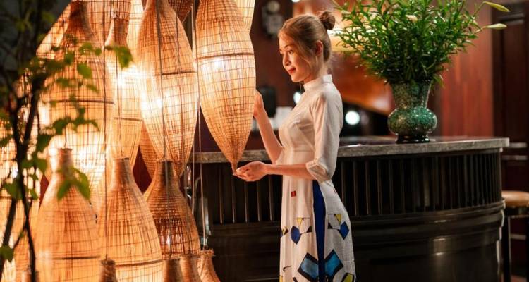 Elegantly dressed woman admiring warmly lit woven lanterns inside an atmospheric interior