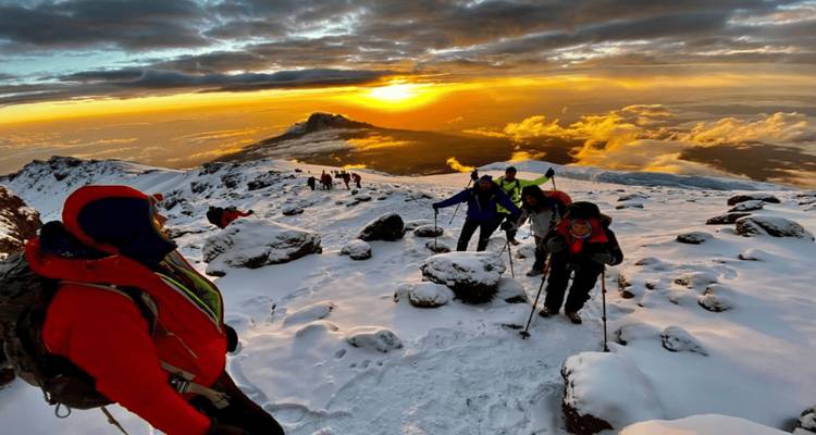 Alpinistes sur montagne enneigée au lever du soleil, ciel coloré.