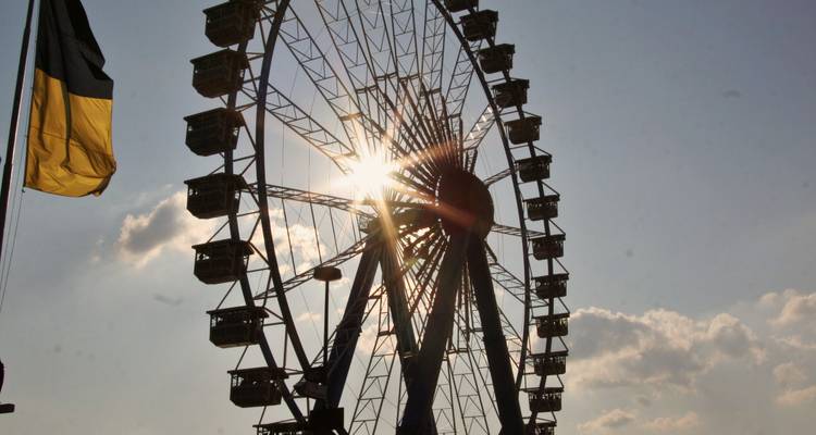 Grande roue avec le soleil derrière elle et un drapeau en vue.