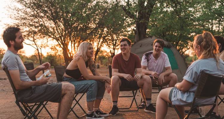 Groupe de personnes assises en train de discuter dans un camping au coucher du soleil.